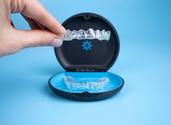 Fingers holding Invisalign tray over its branded case