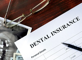 Top of dental insurance form on desk next to X-ray image, pen, and glasses