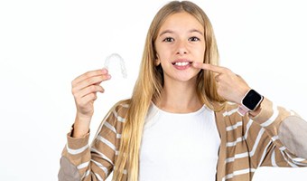 Adolescent girl holding Invisalign aligner and pointing at her teeth